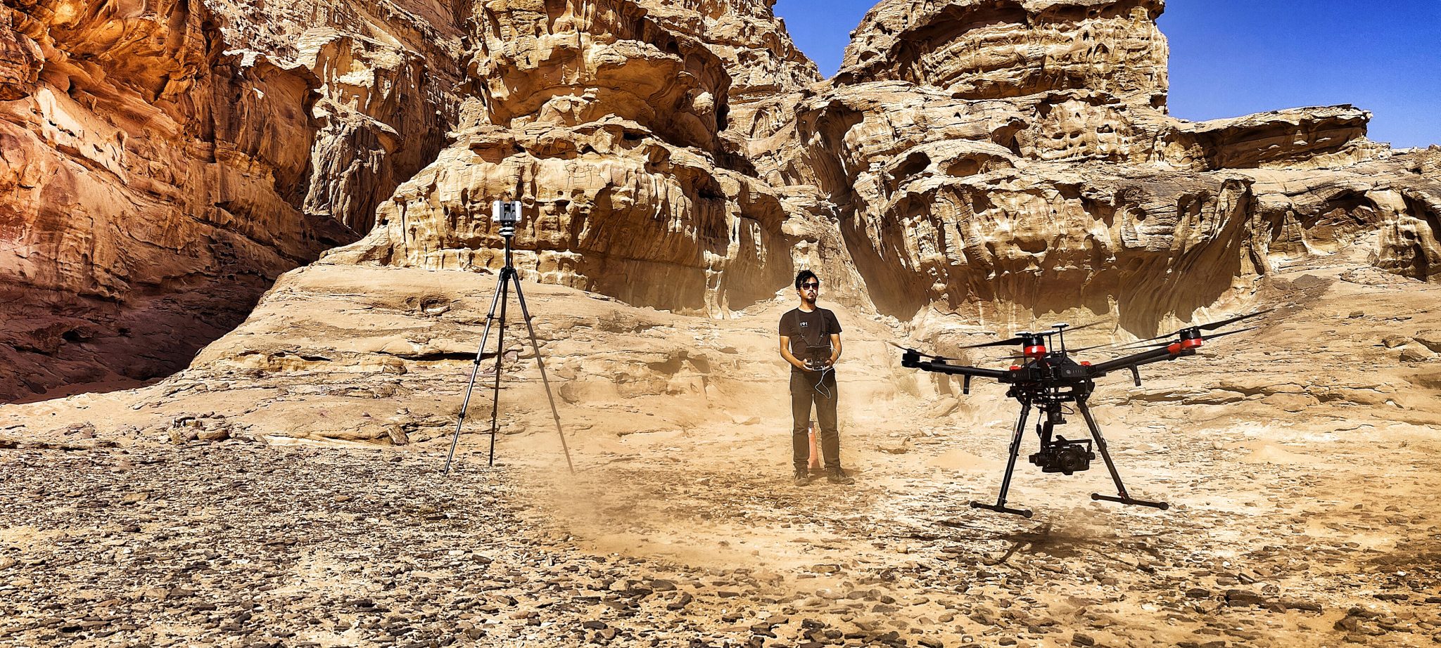 A technician in front of a cliff in the desert, flying a drone equipped for photogrammetry capture, next to a LiDAR scanner.